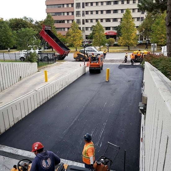 Asphalt being rolled by machinery over newly installed heating cables in a parking garage ramp.